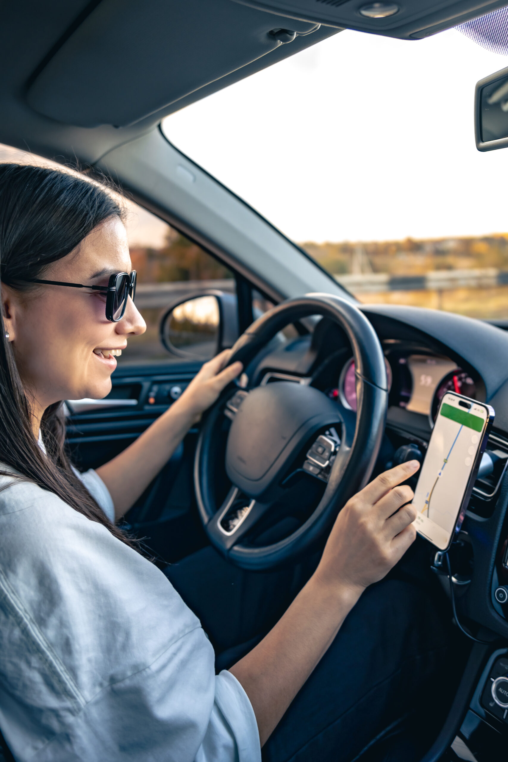 An attractive young woman driving a car uses a navigator in her smartphone.